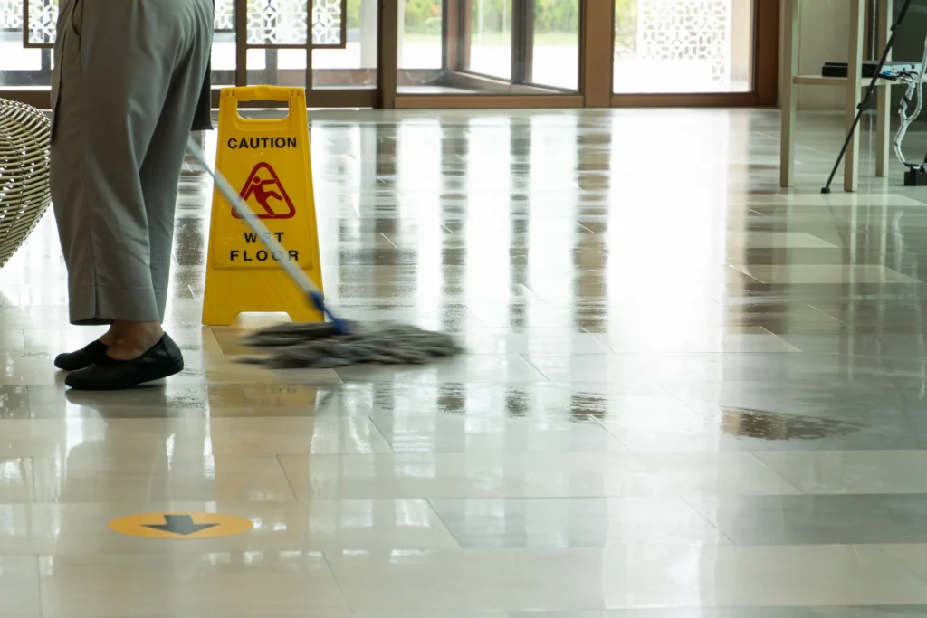 A person mopping the floor and a caution wet floor sign 