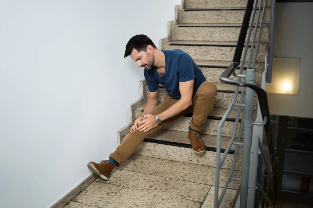 A guy hurt, holding his knee while sitting on the stairs.