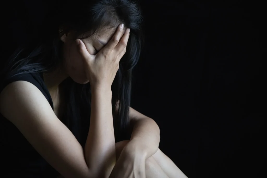 A woman sitting in the dark with her head in her hand, representing the emotional toll of the legal process in a sexual assault case in Austin.